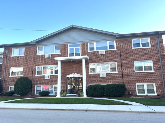 Front view of a three-story brick building with a gabled roof and a central entrance with columns.