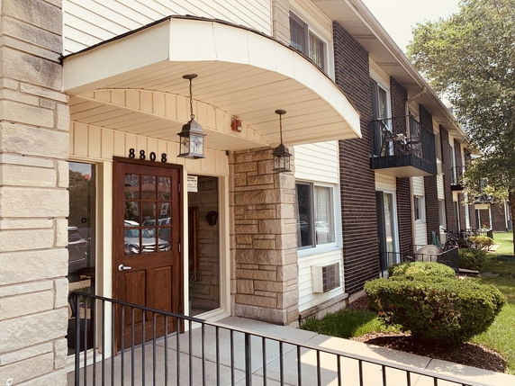 Front view of a two-story building with stone and brick exterior, featuring a wooden door and balconies.