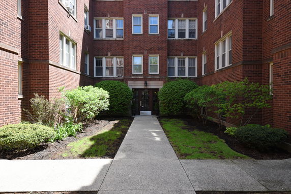Front view of a brick apartment building with a pathway and shrubs.