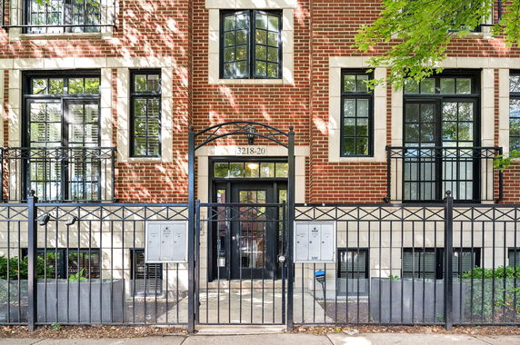 Front view of a brick residential building with black framed windows and a gated entrance.