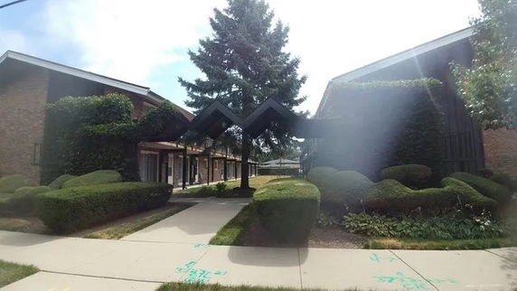 Front view of a building with a unique triangular entrance and landscaped bushes.