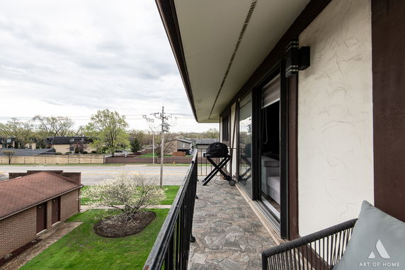 Balcony view from a building with a grill and chairs overlooking surrounding residential area and street.