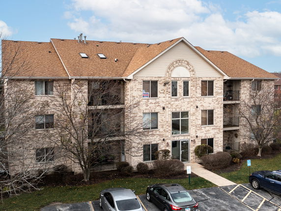 Front view of a multi-story brick building with parked cars in front.