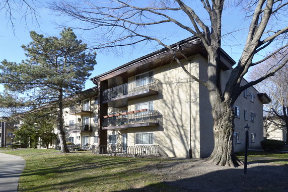 Front view of a multi-story apartment building with balconies and surrounding trees.