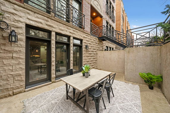 View of a building with stone facade and large windows, featuring a small outdoor patio area with a table and chairs.