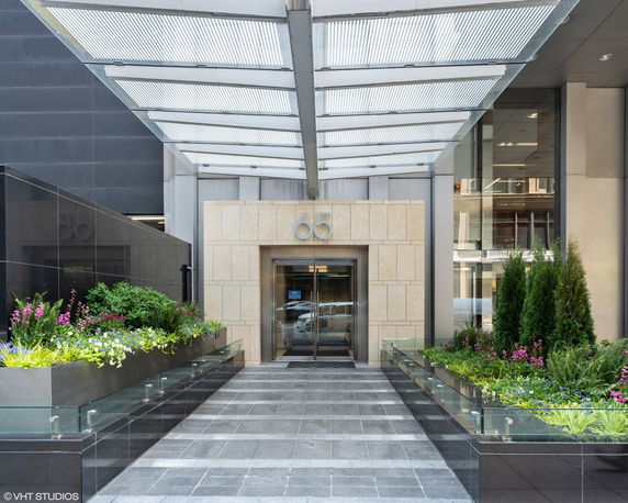 Entrance view of a modern building with glass canopy and potted plants.