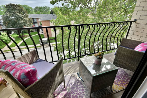 View from a balcony with wicker chairs and table, overlooking trees and rooftops.