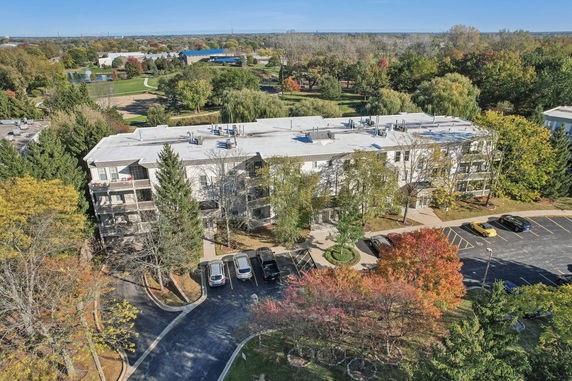 Aerial view of a multi-story residential building surrounded by trees and parking spaces.