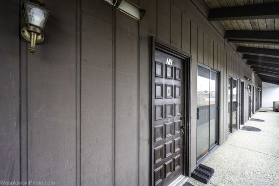 View of an exterior hallway with multiple doors and windows, covered by an overhang.