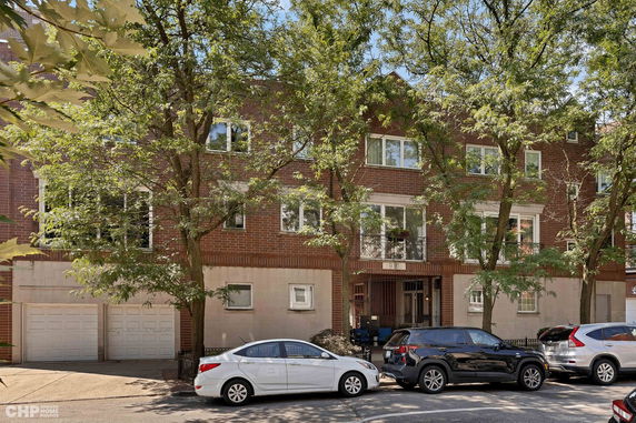 Front view of a multi-story brick building with garages and trees in the foreground.