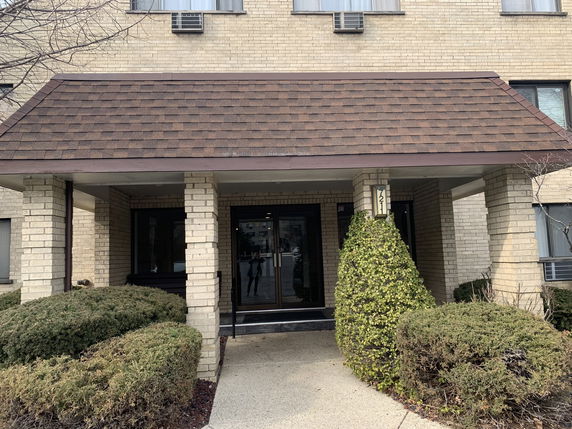 Front view of a brick building entrance with a gabled roof and glass doors.
