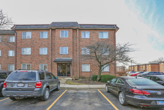 Front view of a three-story brick apartment building with parked cars in front.