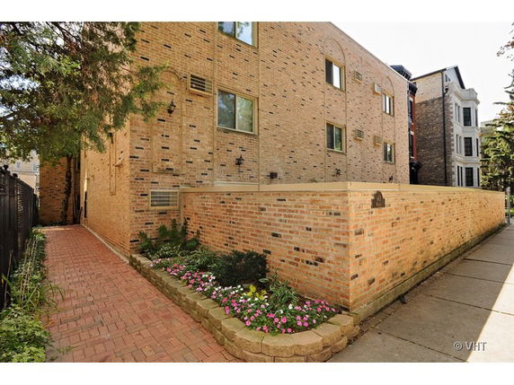 Side view of a brick residential building with multiple windows and a small landscaped area.