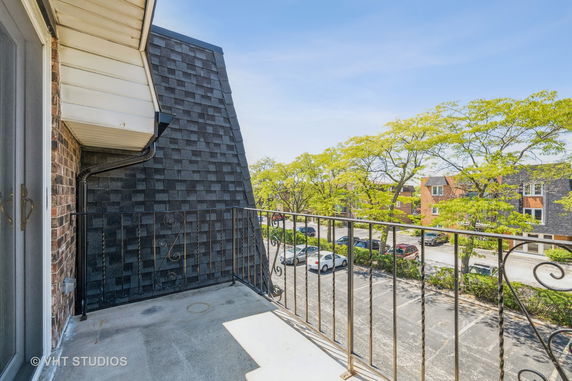 View from a balcony overlooking a parking area with trees and adjacent buildings.