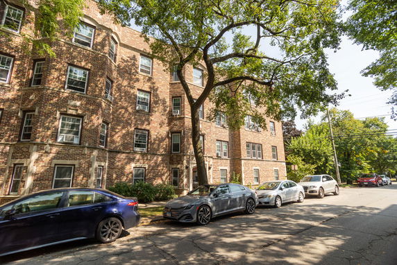 Front view of a multi-story brick building with multiple windows and parked cars in front.