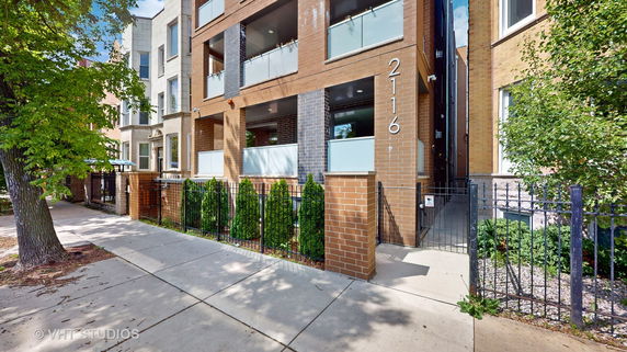 Front view of a modern multi-story brick building with balconies and a gated entrance.