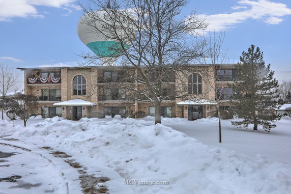 Front view of a three-story building with a central entrance, surrounded by snow. An overhead water tower is visible in the background.