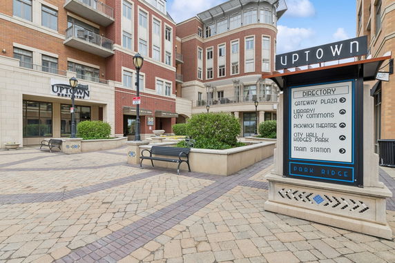 Front view of a multi-story building complex with brick and stone facade, featuring commercial signage and a pedestrian walkway.