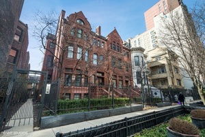 Front view of a red brick multi-story building with ornate architectural details and wrought iron fence.