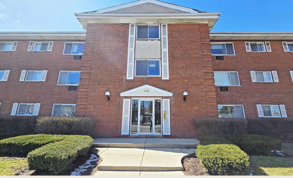 Front view of a multi-story brick building with a central entrance and multiple windows.