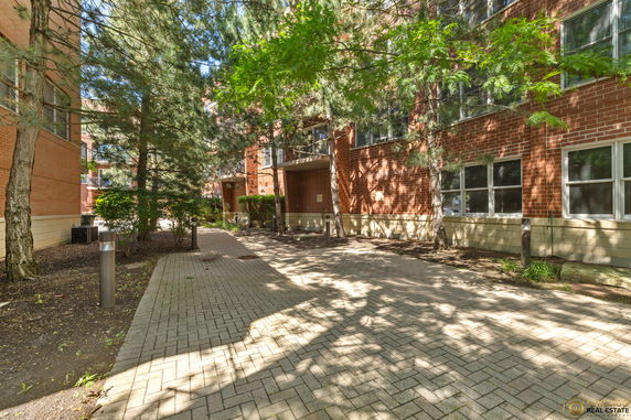 Exterior view of a brick building with paved walkway and trees.