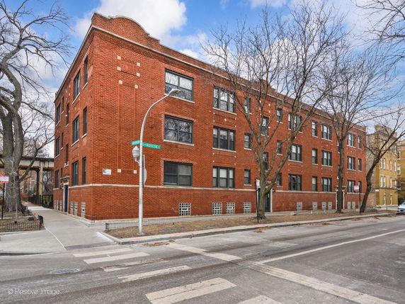 Front view of a three-story red brick apartment building at a street corner.