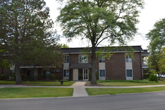 Front view of a two-story brick apartment building with large trees in front.