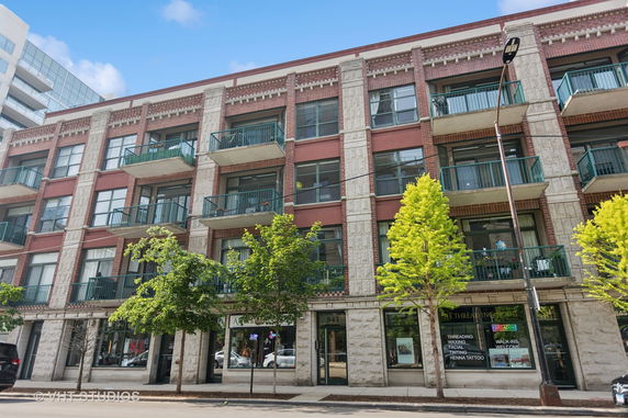 Front view of a multi-story building with balconies and shops at the ground level.