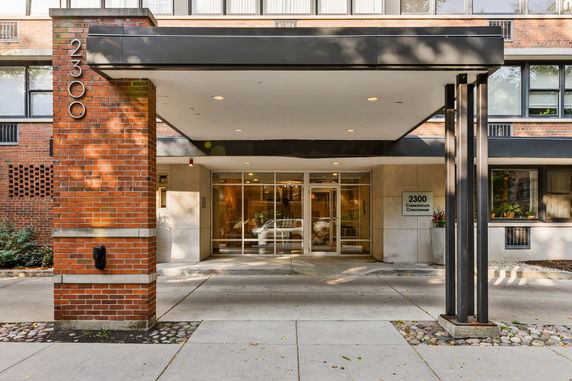 Front view of a building entrance with brick and glass exterior, featuring a covered entryway.
