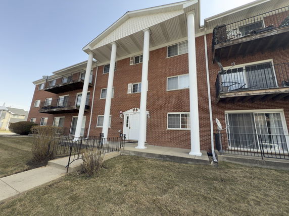 Front view of a three-story brick apartment building with balconies and large white columns.