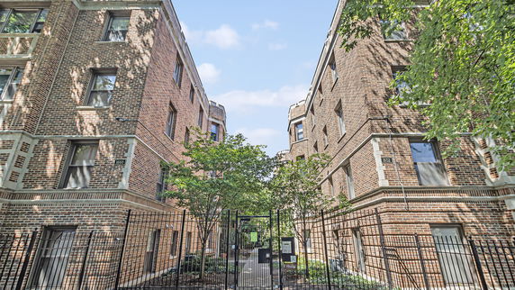 Front view of brick apartment buildings with multiple windows and gated entrance.