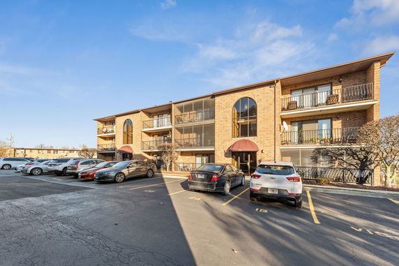 Front view of a three-story brick building with balconies and parking area.
