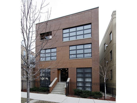 Front view of a three-story brick building with large windows and a stairway entrance.