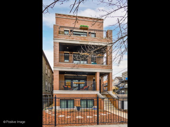 Front view of a three-story brick building with balconies and a fenced yard.