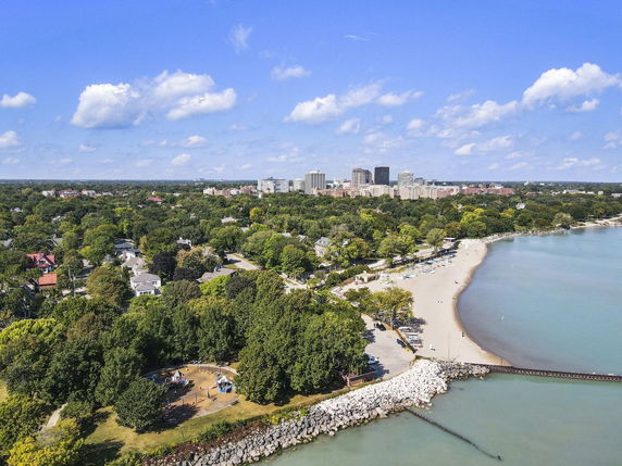Panoramic view of a coastal area with a beach, residential houses, and city buildings in the background.