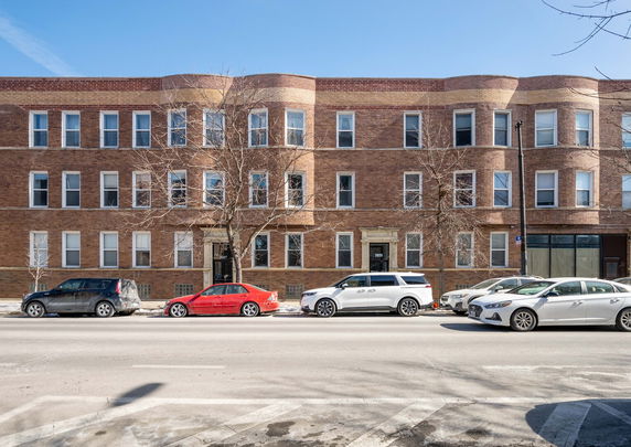 Front view of a multi-story brick building with several windows and parked cars in front.