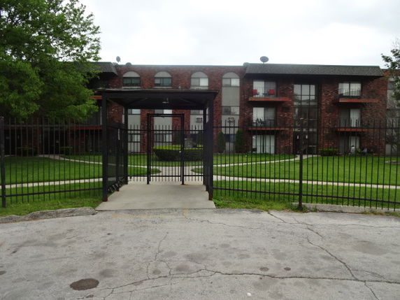 Front view of a multi-story brick apartment building with gated entrance.