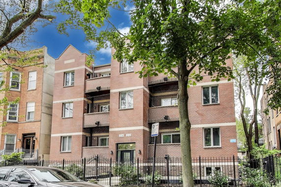 Front view of a multi-story brick apartment building with balconies and a fenced entrance.