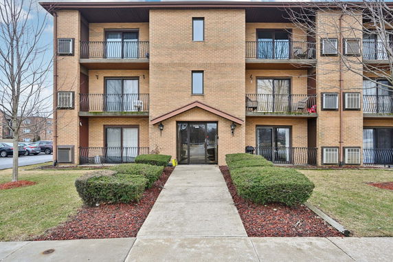 Front view of a three-story brick apartment building with balconies.