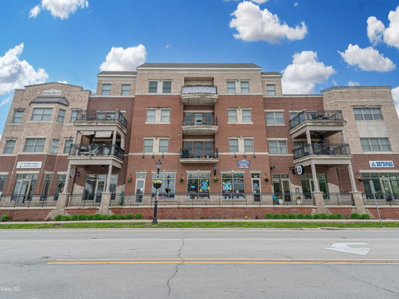 Front view of a multi-story brick building with balconies and several commercial spaces at street level.