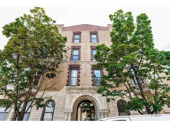 Front view of a multi-story brick building with large trees partially obscuring the facade.