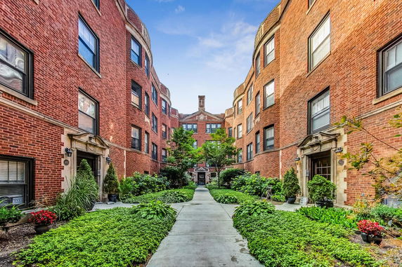Front view of a red brick apartment building with multiple windows and a landscaped walkway.