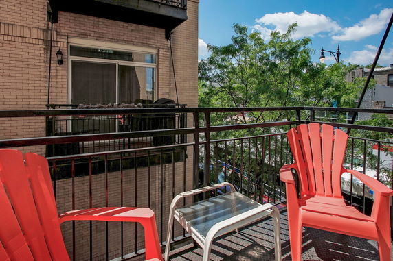 Balcony with red chairs and a small table overlooking city surroundings and trees.