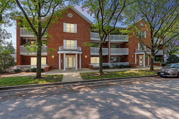 Front view of a multi-story brick building with balconies and a tree-lined street.