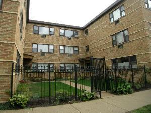 Front view of a multi-story brick apartment building with a fenced entrance.