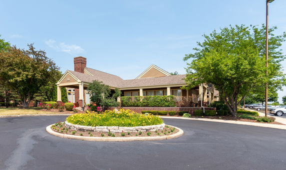 Front view of a single-story house with a brick chimney and a roundabout driveway.
