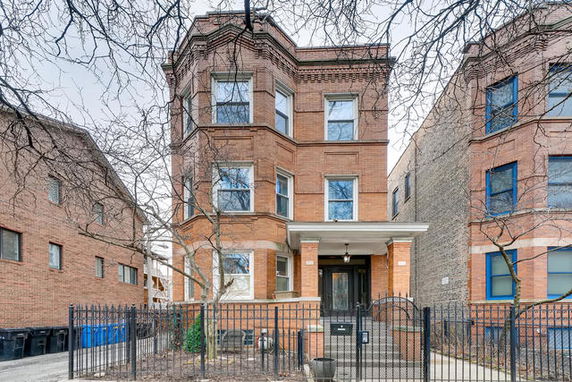 Front view of a three-story brick building with a gated entrance.