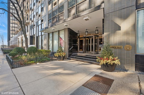 Front view of a modern multi-story building entrance with glass doors and decorative plants.