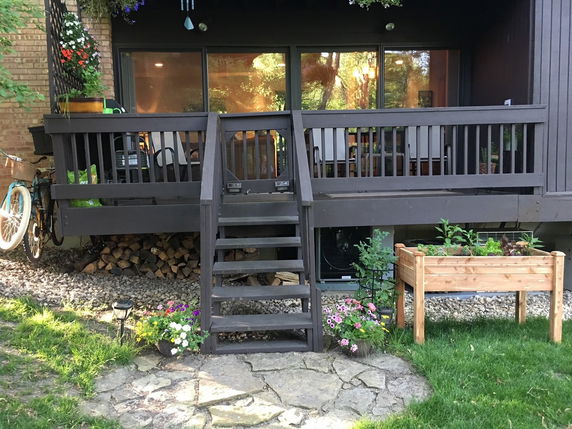 Rear view of a house with a raised wooden patio, staircase, and sliding glass doors.