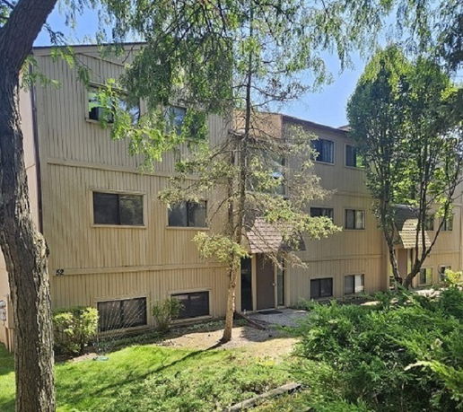 Front view of a multi-story residential building with multiple windows and surrounded by trees.